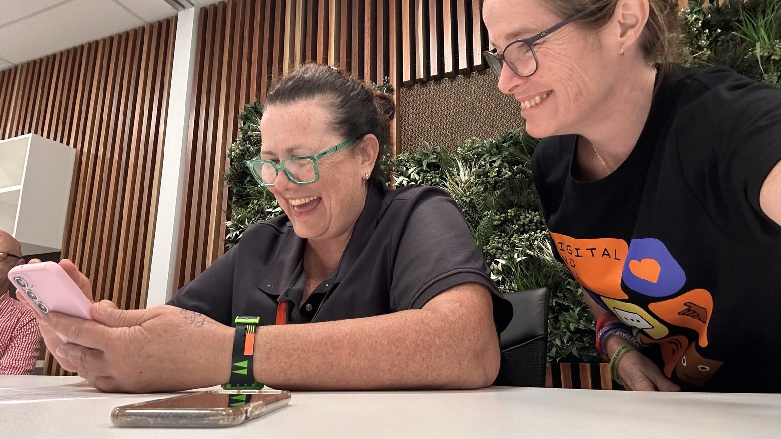 A workshop participant in Julia Creek laughing at her own phone screen while Suzie leans in beside her